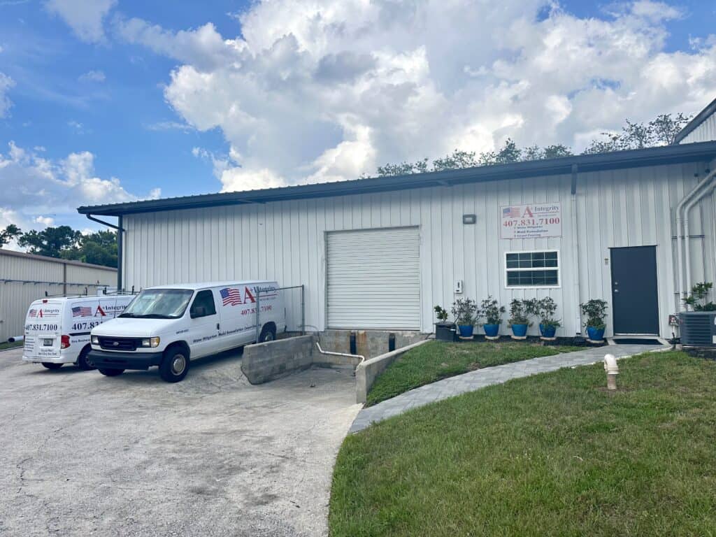 Restoration and water damage repair building with branded vehicles parked outside, featuring a large white garage door, potted plants, and a well-maintained lawn, emphasizing professional restoration services.