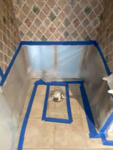 Bathroom water damage repair with protective coverings during restoration process. Water damage restoration preparation in bathroom with plastic sheeting and blue painter’s tape for mold prevention and moisture control.