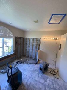 Restoration service for water and mold damage in a bathroom undergoing renovation, including drywall removal, wall drying, and mold remediation by A+ Integrity Restoration. Damaged bathroom remodel under construction showing exposed wall framing, air vent installation, and construction tools in progress.