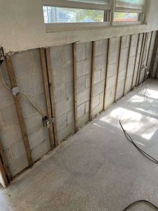 Restoration of water-damaged walls and drywall repair services by A+ Integrity Restoration. Damaged wall undergoing restoration with exposed wood framing and electrical wiring for water damage and mold remediation.
