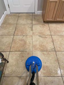 Restoration of tiled kitchen flooring after water damage with professional cleaning services. Deep cleaning of ceramic tile floor in kitchen, showing professional pressure washing in progress for mold and dirt removal.